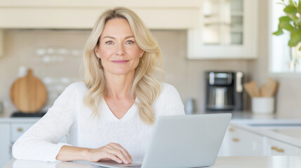 Smiling woman works happily from home on her laptop at a cozy kitchen table, exuding confidence and comfort in a modern interior setting