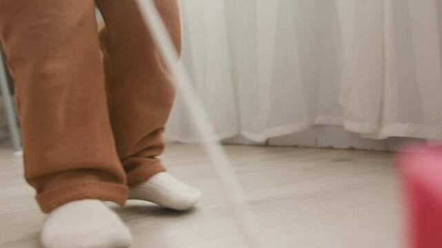 Low part of legs of little child wearing brown pants and white cotton socks pulling rope with toy while moving backwards on the floor along domestic room