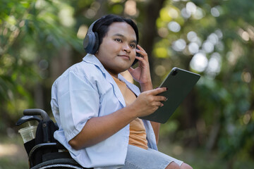Young Man in Wheelchair Using Tablet and Headphones for Online Work in Outdoor Setting