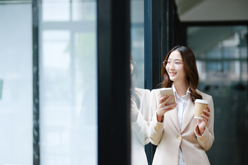 Businesswoman smiling while holding a coffee cup and checking her phone during a work break