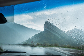 A wet road on a cloudy and rainy day seen from inside a vehicle. There is a dangerous curve with low visibility. Concept of driving, transportation and caution on the road © LaMorenita