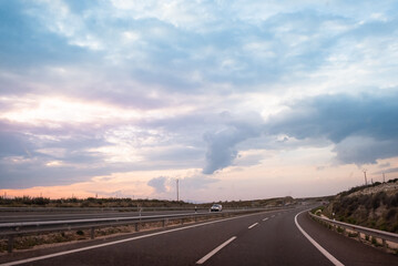 Panoramic view of a highway at sunset. The sky is cloudy and stormy and the colors of the sunset give a watercolor look to the overall panorama. Freedom, travel and transportation concept