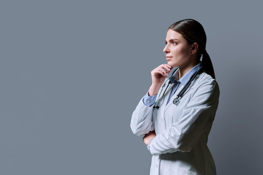 Profile view of young female doctor with stethoscope on gray background