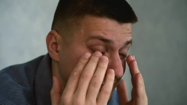 A man rubs his eyes with his hands.
A foreign object got into the person's eyes and caused discomfort.
The guy's eyes are watering.
Discomfort in a person's eyes