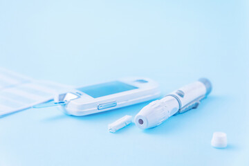 Diabetes mellitus. Close-up of lancet and glucometer - medical devices for self-monitoring of blood glucose levels on a blue background with copy space. Problems of diabetes mellitus in pregnant women