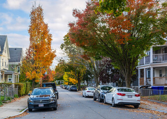 Residential street scene with autumn foliage and parked cars in Brighton, Massachusetts, USA
