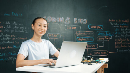 Smart girl programing system by using laptop at blackboard. Highschool student writing engineering code or prompt while looking at camera at STEM technology class. Creative education. Edification.
