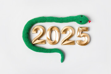 Knitted toy striped green snake and gold numbers. Symbol of the year 2025 on gray background.