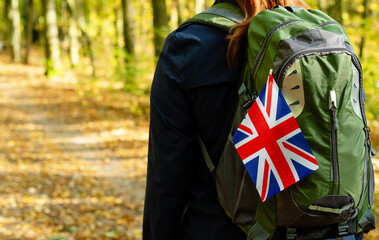 Woman with a backpack and a British flag walking along a forest road, close-up, view from the back....