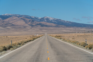 U.S. Route 50, the loneliest road in the USA, view towards snowcapped mountains. Empty road and clear blue sky.