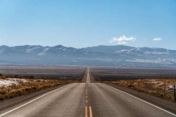 U.S. Route 50, the loneliest road in the USA, aerial view towards snowcapped mountains. Empty road and clear blue sky.	