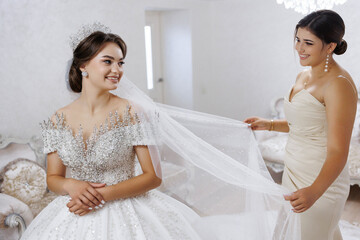 A bride is getting ready for her wedding and her bridesmaid is helping her with her veil