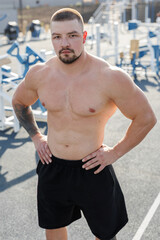 Obraz premium Young handsome bodybuilding athlete poses against the background of modern sports ground at sunset.
