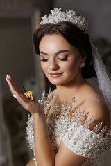 A woman is holding a butterfly in her hand. She is wearing a gold tiara and a white dress