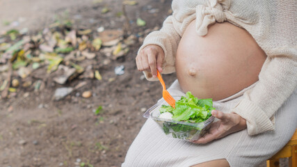 Closeup of pregnant woman holding vegetable salad in hand While using a fork to poke down to eat, food control during pregnancy