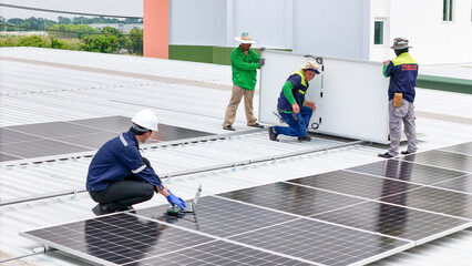 A team of technicians inspects solar panels on metal rooftop, equipped with tools, laptops, and...