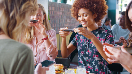 Group Of Young Female Friends Taking Photos Of Food In Restaurant To Post On Social Media