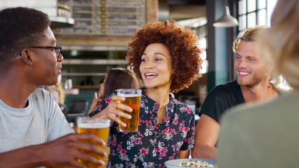 Group Of Young Smiling Friends Sitting At Table Meeting For Drinks In Bar 