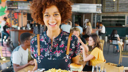 Portrait Of Female Server In Busy Bar Restaurant Smiling At Camera