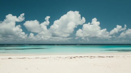 Obraz premium A pristine white sand beach stretches towards a turquoise ocean, with a clear blue sky and fluffy white clouds overhead.