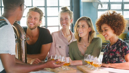 Male Server With Group Of Young Friends At Beer Tasting In Bar