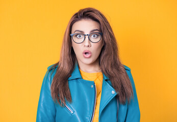 Surprised face of woman stare to camera, wearing blue leather jacket, isolated on yellow...