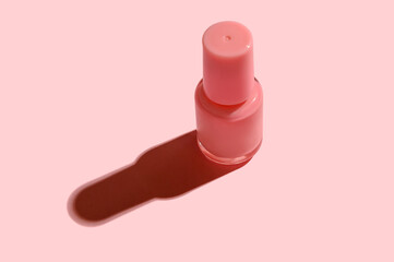 Pink glass container with nail polish on pink background.