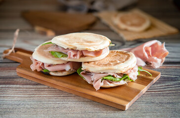 Tigelle with mortadella and rocket on wooden cutting board