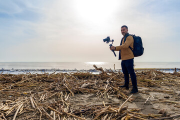Camera Operator Filming Flood-Damaged Vegetation and Debris Washed Ashore on a Beach Using a Gimbal