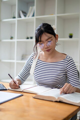 Intelligent young woman having online lessons on laptop, drinking coffee and taking notes,