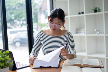 Intelligent young woman having online lessons on laptop, drinking coffee and taking notes,