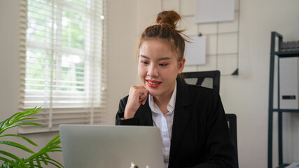 Businesswoman sitting at desk on couch in workplace or at home working on laptop and analyzing data on charts and graphs and writing on papers to make business plan