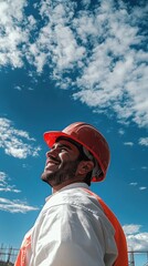 Smiling Hispanic male construction worker in hard hat against a bright blue sky.