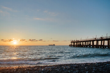 Fototapeta premium A sunset on the beach with crowded pier and a ship on horizon