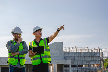 Two construction engineers inspect the progress of a building construction plan at a construction site.