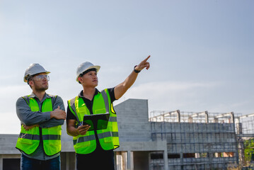 Two construction engineers inspect the progress of a building construction plan at a construction site.