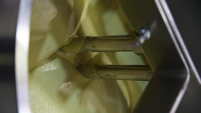 Close-up view of working of modern rotary conche machine. Stirring machine mixes white chocolate mass. Real time handheld vertical video. Soft focus. Confectionery production theme.
