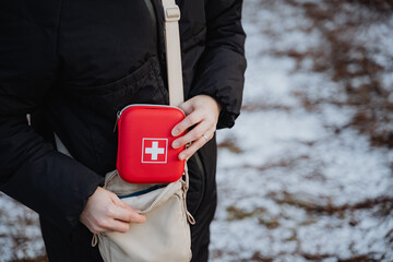 A person is confidently holding a first aid kit in their hand while standing in a location that may...