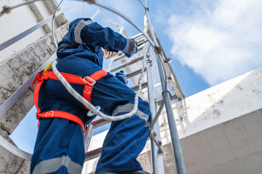 Engineer in Full Safety Gear Climbing a Ladder to Inspect Communication Signals and Industrial Machinery at a High-Risk Transportation Facility