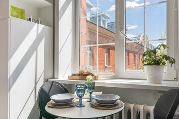 A fragment of the interior of the studio apartment. Elegant table setting. A window with a view of a sunlit brick house on a summer day.