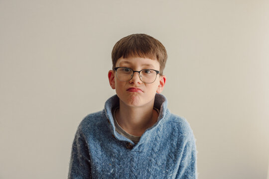 grumpy pre-teenager young boy on neutral background blue jumper, disappointed, annoyed, wearing glasses 11 year old boy