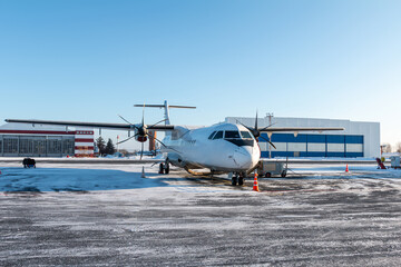 White passenger turboprop airplane on the airport near an aircraft hangar in winter