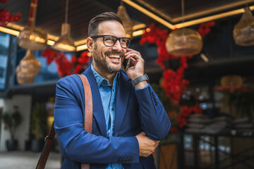 adult businessman stand in front restaurant and talk on mobile phone