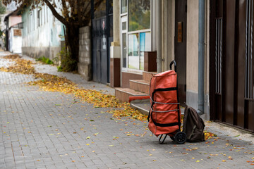 A large red forgotten shopping bag on wheels stands outside on the paving slabs at the gate