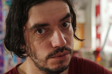 A cheerful man with shoulder-length dark hair beams with joy in a colorful indoor environment filled with vivid decorations, creating a warm atmosphere.