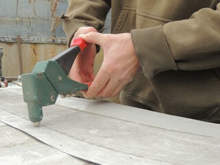 close-up of worker's hands with riveting gun during work, placing rivets on metal using hand-held...