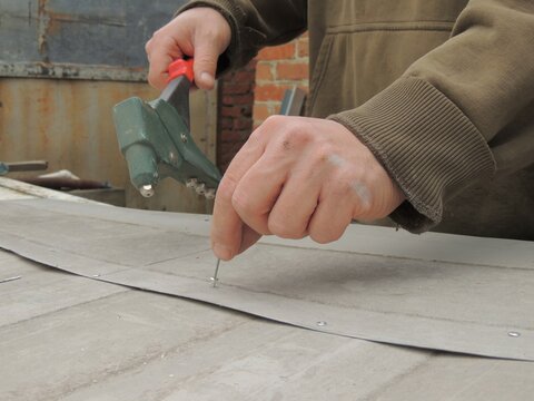 inserting a thin long aluminum rivet into a metal structure, the worker's hands holding the fastener and riveter