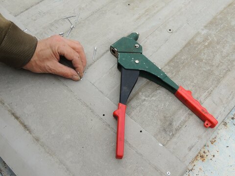 riveting tool on iron texture top view and male hand holding aluminum rivet, hand held device for setting rivets when joining thin metal parts