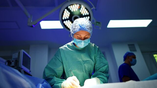 Female surgeon uses metal tool at operation. Low angle view at the professional carrying out surgery alone.