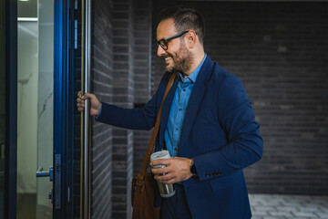 Smiling adult man businessman enter building with cup of coffee